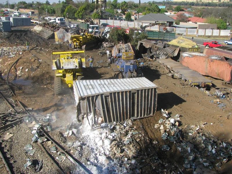 Two earth moving machines pulling out a container filled with some chemical. Scrap loaded into truck in the background plus tangled containers
