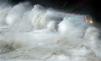 Waves batter a train as it passes along the coastal railway line at Dawlish in Devon, south west England. 27 Oct 2004 REUTERS/Toby Melville