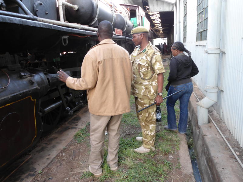 Museum Curator Maurice Barasa explains the workings of a steam loco to the Director of Nairobi National Park, while the media hang around in the background. Kenya Wildlife Service is a major partner in the monthly steam trips.