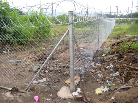 The south eastern fence post, showing the eastern side of the fence stretching towards a metro train in the distance