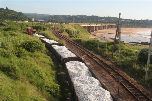 On reportedly the last day of scheduled service, the Port Shepstone shunt is seen propelling loads from the quayside quarry into the station. The river bridge forms the backdrop.