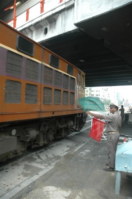 Red flag for traffic and green flag for trains. Level crossing attendant in Bangkok sees his train safely over one of the many manned crossings in the city.