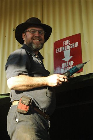 Having reached great heights, Railroad Jones smiles down at the photographer, as he has just completed a new stunt of affixing a warning sign without using a ladder. The weapon in his hands doubles as a drill!