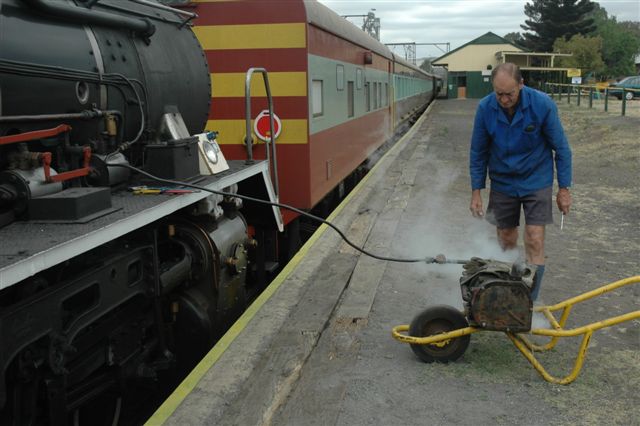 The ingenuity of a fitter! Robert Dadford devised this system of bench (wheelbarrow chassis) testing a locomotive dynamo, after refurbishing it. Steam is taken from an extension pipe, coupled to the reverser steam and then, via a regulating valve, steam enters the dynamo. He then has electrical connections leading to a sealed beam headlight and two cab globes mounted on a wooden frame. There is a voltmeter fitted, and the settings are made to reach 32v operating current. Simple isn't it?!
