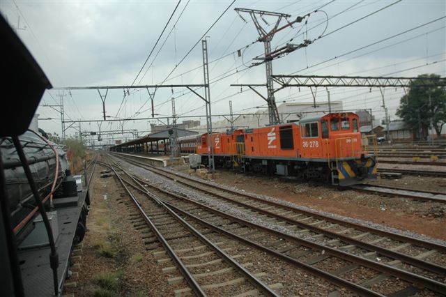 Paper and rubbish lying about makes an interesting approach to Pretoria main station. The gloomy day is broken by the vivid orange of the class 36 shunt locomotives. Some red and grey stock can be seen in the background. Viewed from the Rovos Rail class 119D number 3360.