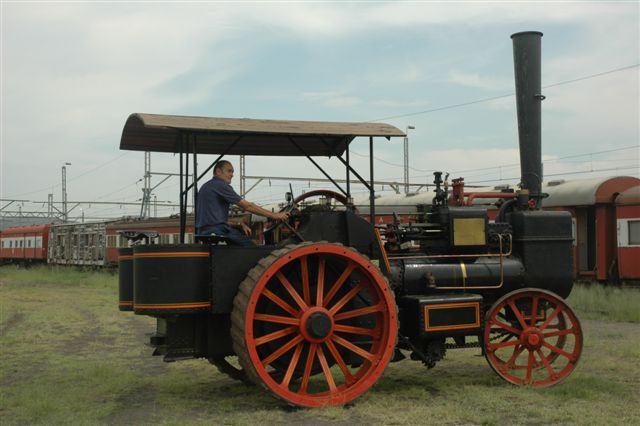 Robert Dadford gracefully gets the steam tractor to turn amongst the parked cars at the Hercules site. The collection of carriages line up in the background, to witness the "driving" test!